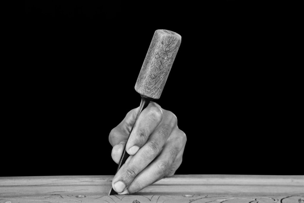 Artistic black and white close-up of a hand using a chisel for wood carving.